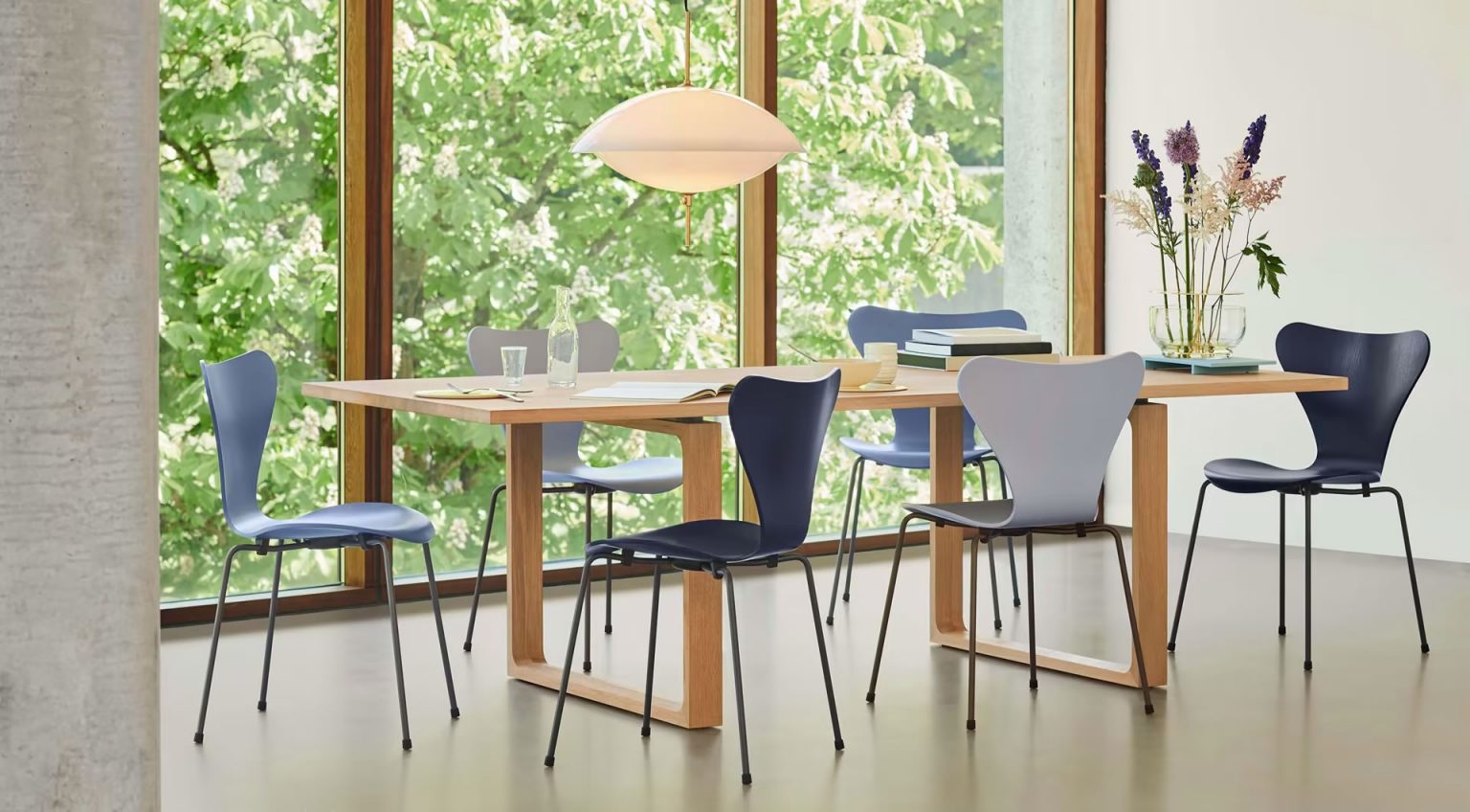 Fritz Hansen Serie 7 Stühle in Blau und Grau um einen Esstisch aus hellem Holz, mit moderner Pendelleuchte und Blick ins Grüne – skandinavisches Wohnambiente bei Loeser Braunschweig