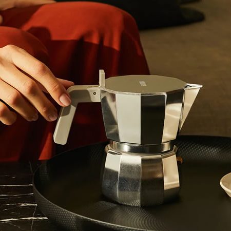 Alessi Moka Espressokanne aus Aluminium auf schwarzem Tablett neben Espressotasse – klassisches italienisches Design für stilvollen Kaffeegenuss
