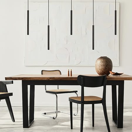 Schlanke schwarze Baltensweiler Pendelleuchten über einem Esstisch aus Holz mit Wiener-Geflecht-Stühlen – elegantes Zusammenspiel von Licht, Form und Material im modernen Interieur