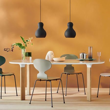 Fritz Hansen Serie 7 Stühle in sanften Grüntönen um einen hellen Holztisch mit schwarzer Pendelleuchte und Dekoration – harmonisches skandinavisches Wohnambiente