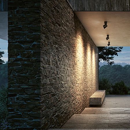 Moderne IP44.de Außenstrahler beleuchten eine Natursteinwand und schaffen stimmungsvolles Licht im überdachten Eingangsbereich mit Blick in die Landschaft
