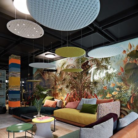 Farbenfroher Wohnraum mit modernen Nimbus Pendelleuchten und Akustikpaneelen, kombiniert mit Pflanzen, Mustertapete und Designer-Sofas – inspirierendes Interior mit spielerischer Lichtgestaltung