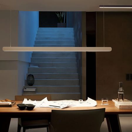 Occhio Mito linear Pendelleuchte über einem großen Holztisch mit Zeichnungen und Accessoires – elegantes, minimalistisches Lichtdesign in architektonischem Umfeld