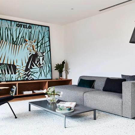 Graues Prostoria Sofa mit minimalistischer Formensprache in modernem Wohnzimmer mit Kunstwerk, Holzdetails und Designer-Stehlampe – zeitgenössisches Interieur mit Stil