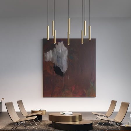 Minimalistische Ribag Vertico Pendelleuchten in Gold über stilvoller Sitzgruppe mit Kunstwerk und Panoramafenster – edles Lichtkonzept für moderne Wohn- und Geschäftsräume